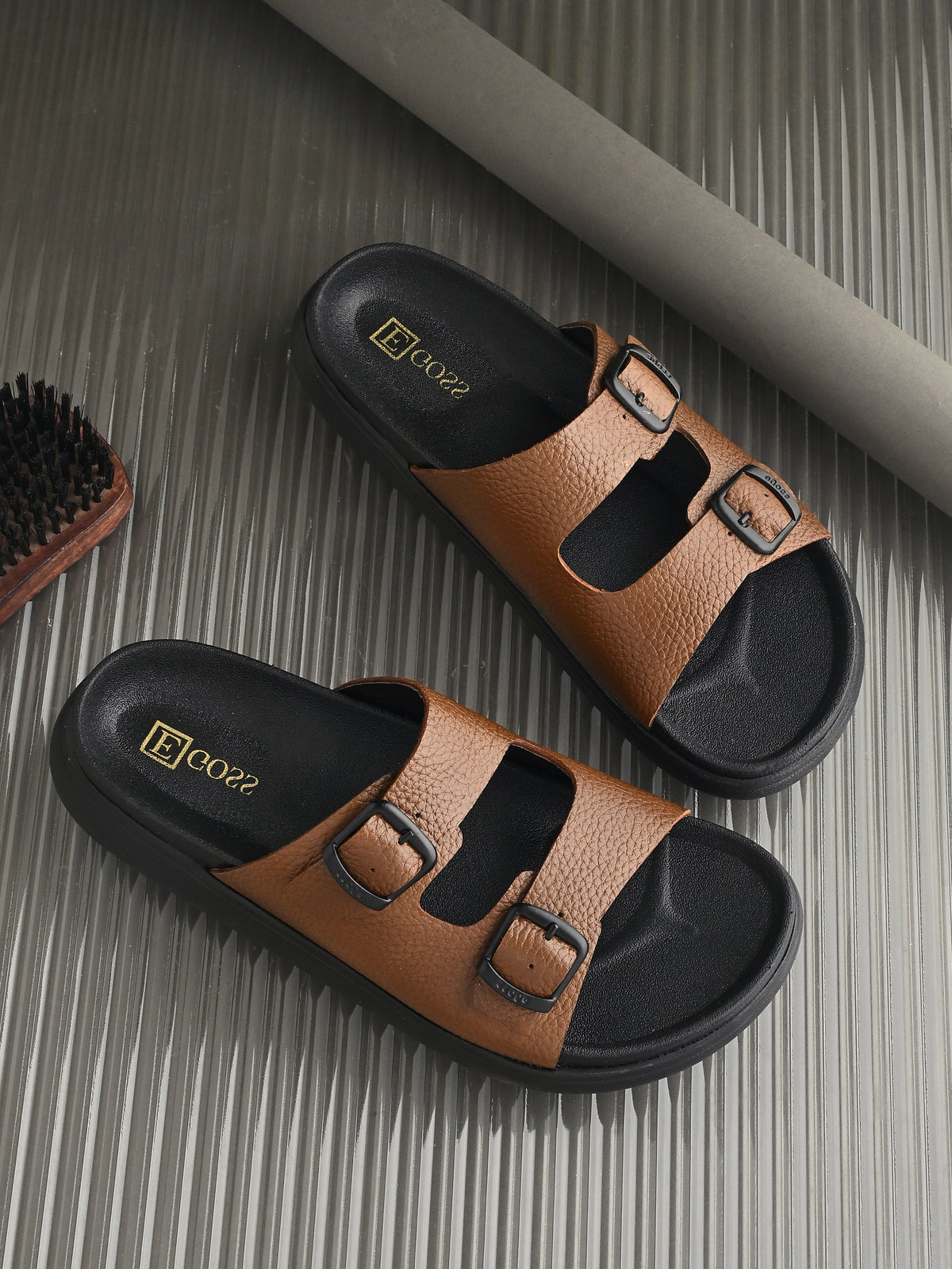 Pair of brown sandals with black soles on a textured surface