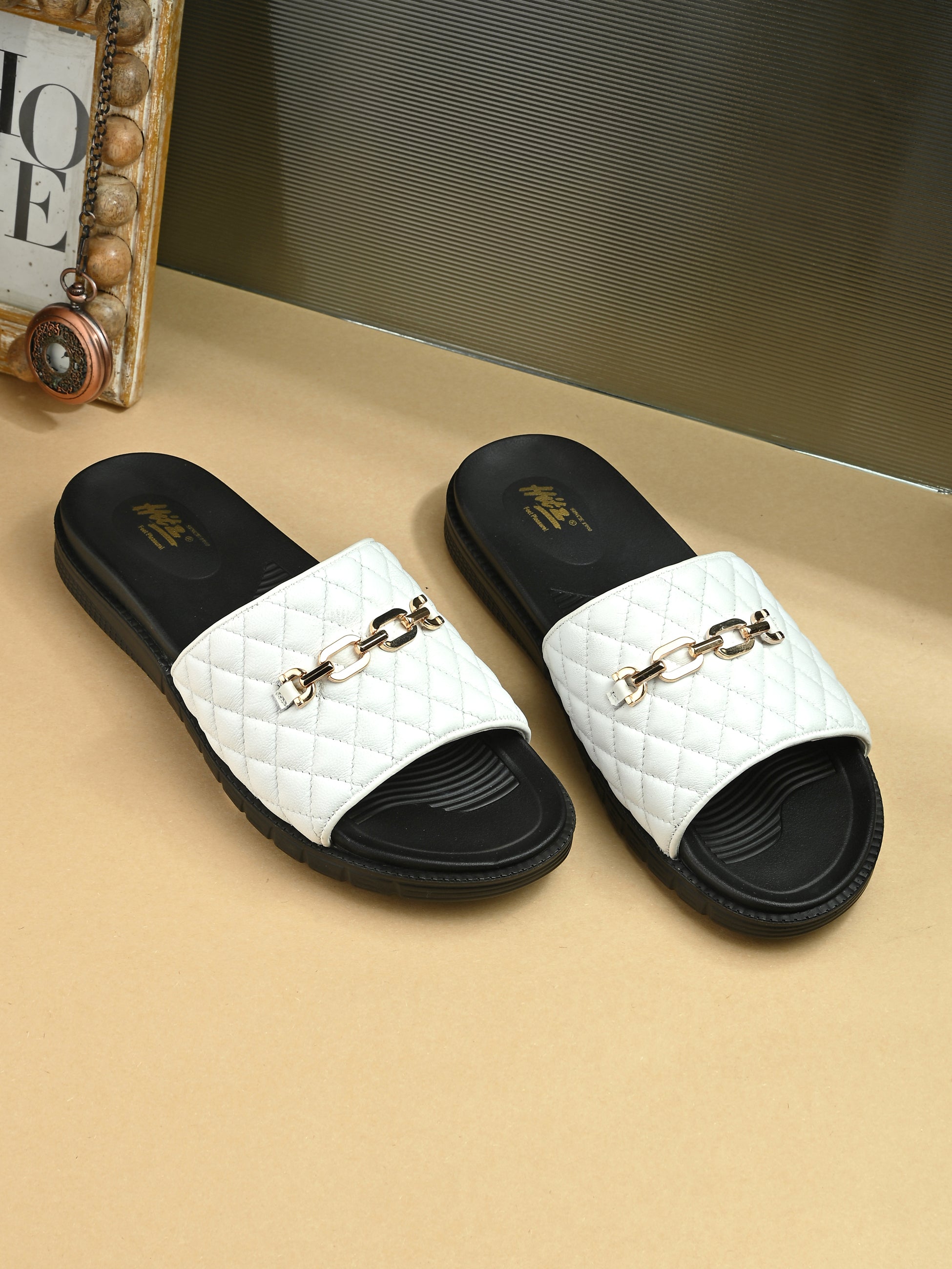 White quilted slide sandals with gold buckles on a beige surface.