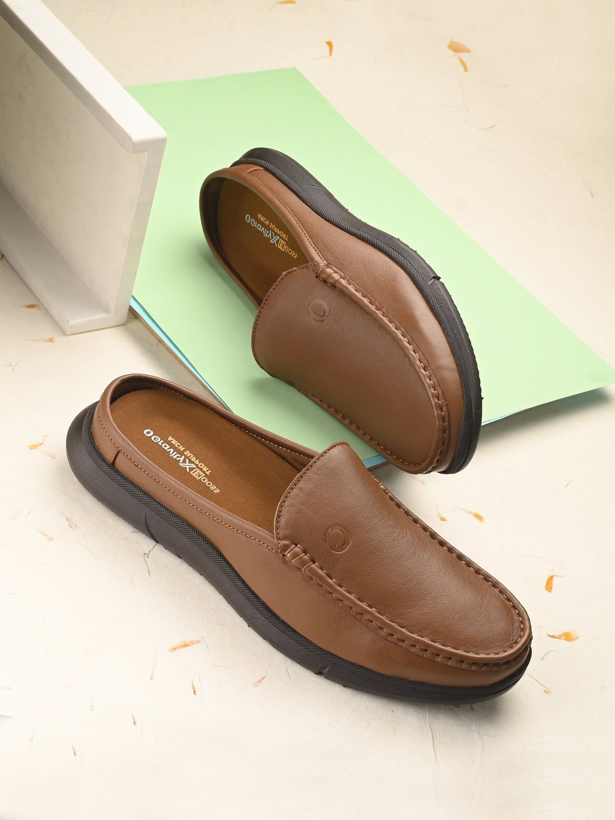 Brown leather loafers on a light background with a green paper and white box.