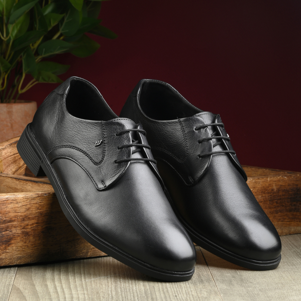 Pair of black leather dress shoes on a wooden surface with a blurred background