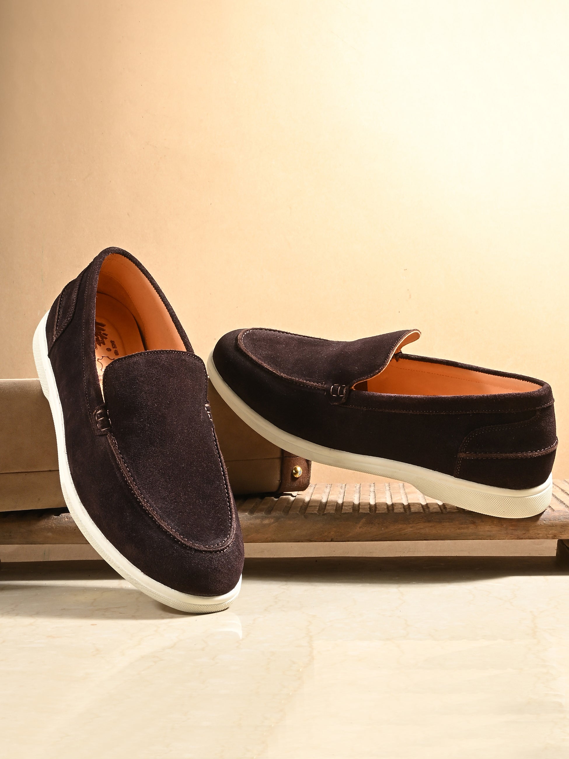 Pair of brown loafers with white soles on a wooden surface.