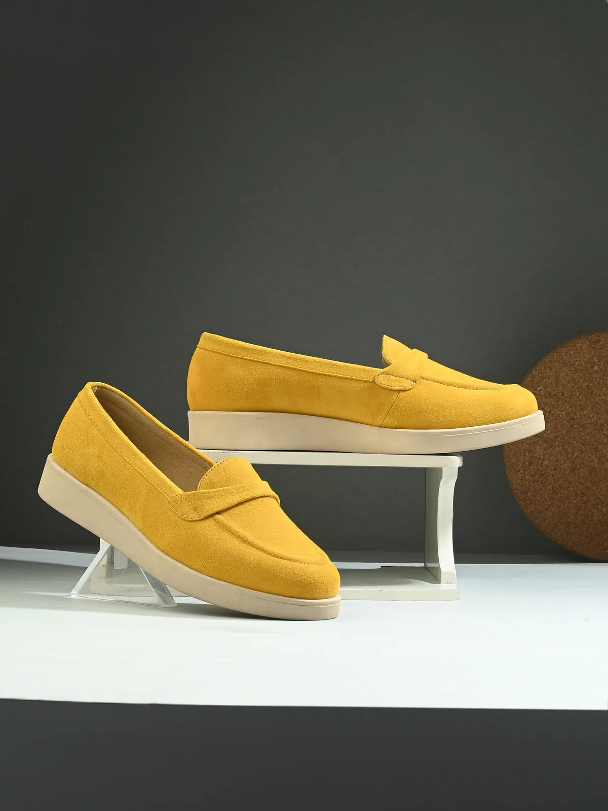 Yellow loafers on a white stand against a dark background