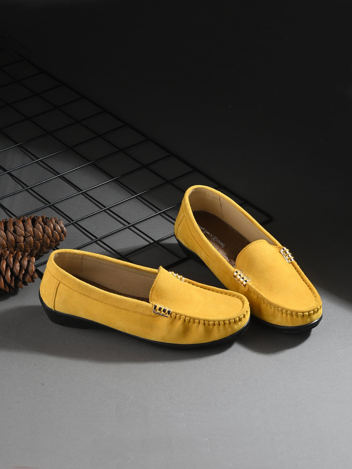 Yellow loafers on a dark surface with a pine cone