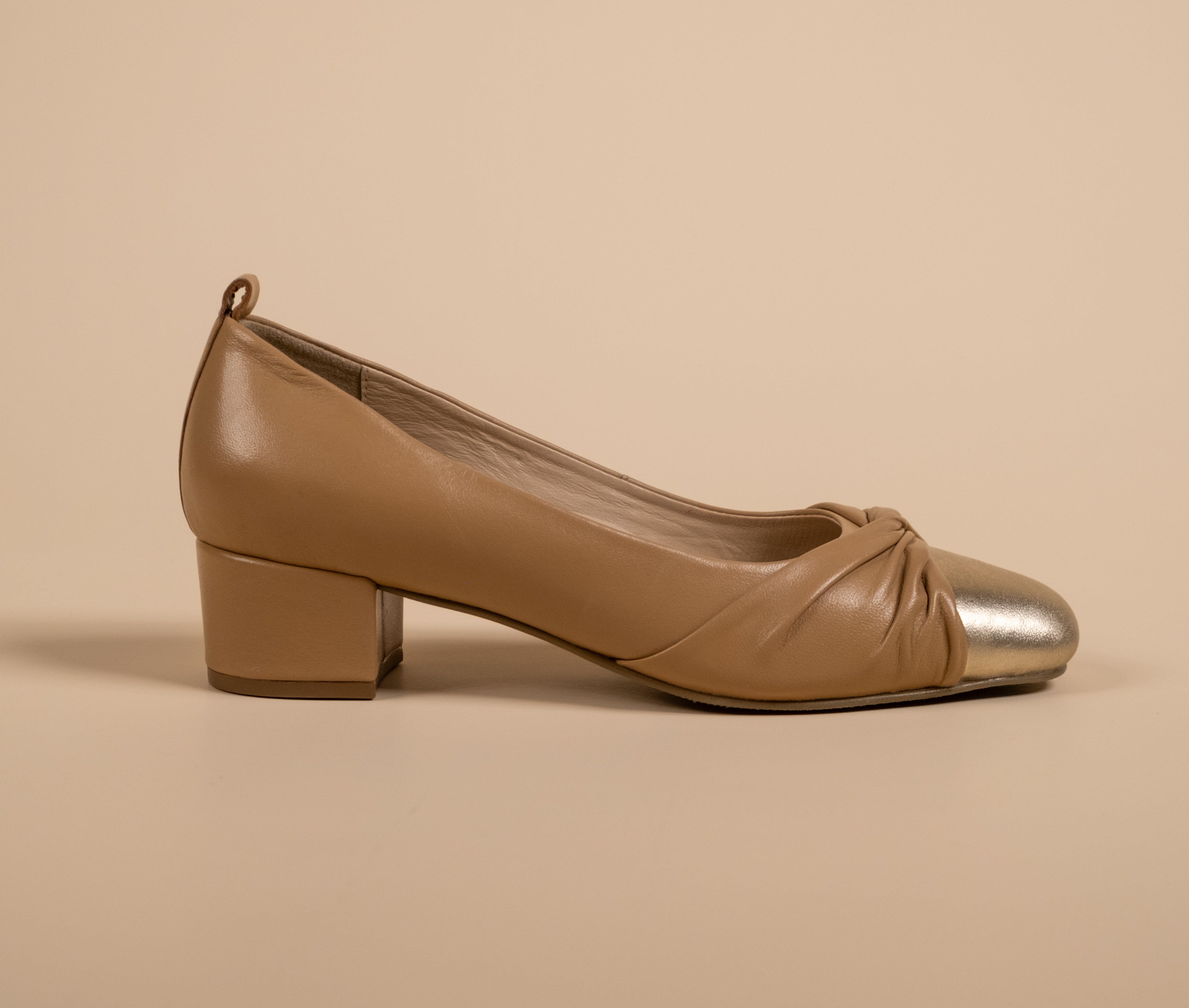 Tan shoe with metallic cap toe on a beige background